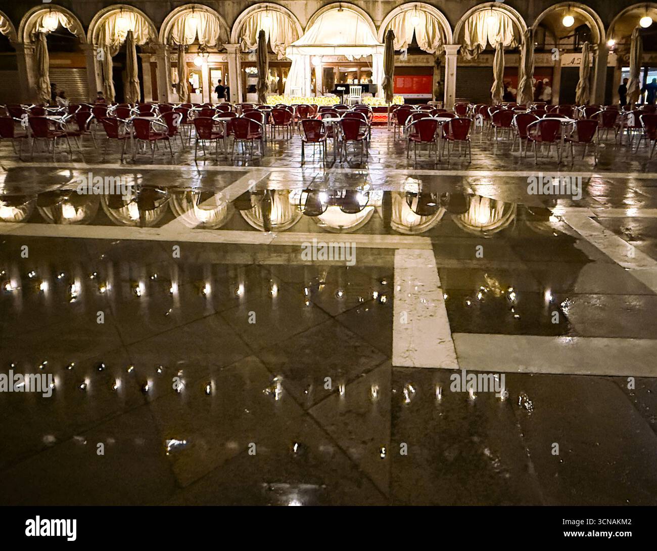 Exterior of the historic Gran Caffè Quadri in St Mark's Square, reflected in the water of a puddle after a storm, at night, Venice, Veneto, Italy - Smartphone Captured Stock Image