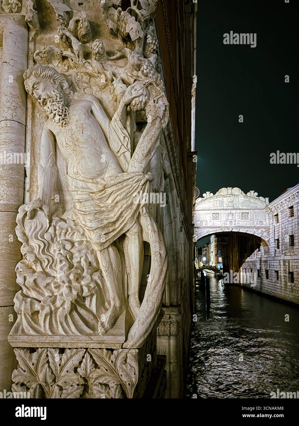 Bas-relief depicting  the biblical episode of Noah’s Drunkenness on a corner of Doge’s Palace with Bridge of Sights in the background at night, Venice - Smartphone Captured Stock Image