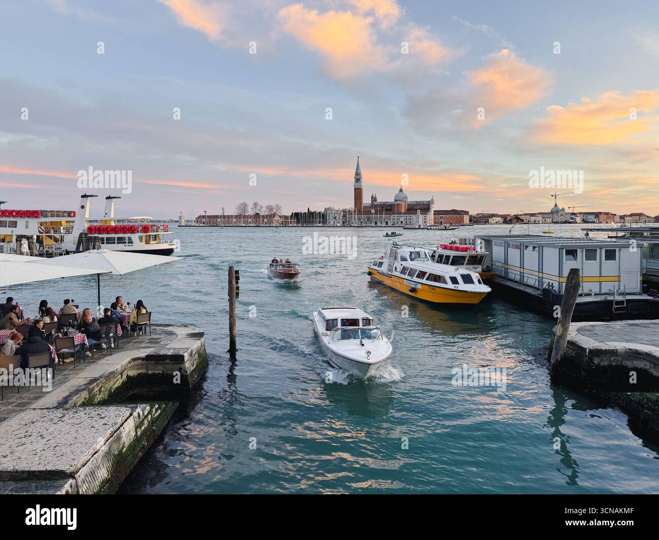 Sunset view of the St Mark's Basin from Ponte della Pietà, with people in a waterfront cafè and the Island of San Giorgio Maggiore, Venice, Italy - Smartphone Captured Stock Image