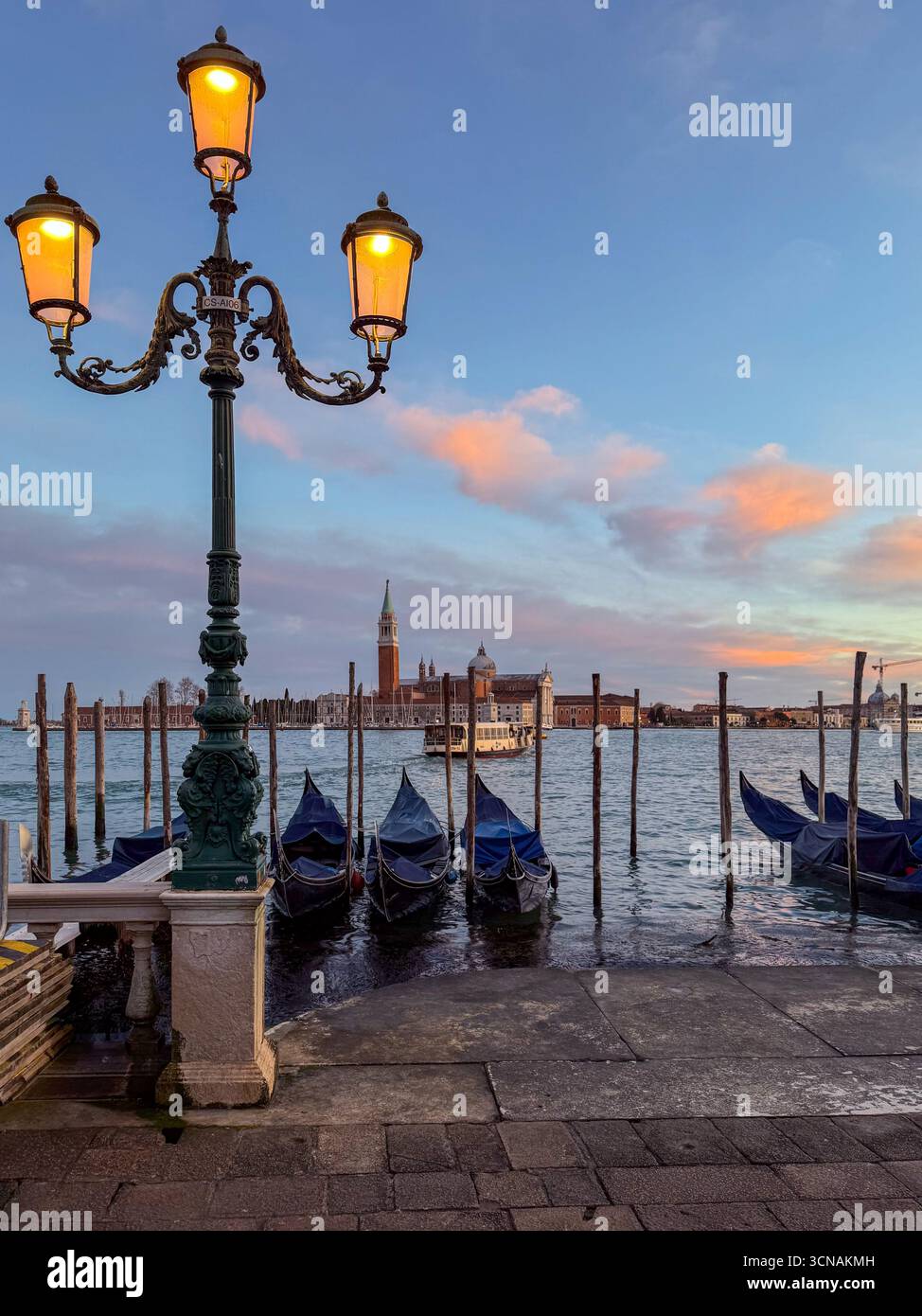 Gondolas moored under a glowing streetlight at Riva degli Schiavoni, with the Island of San Giorgio Maggiore in the background at sunset, Venice Italy - Smartphone Captured Stock Image