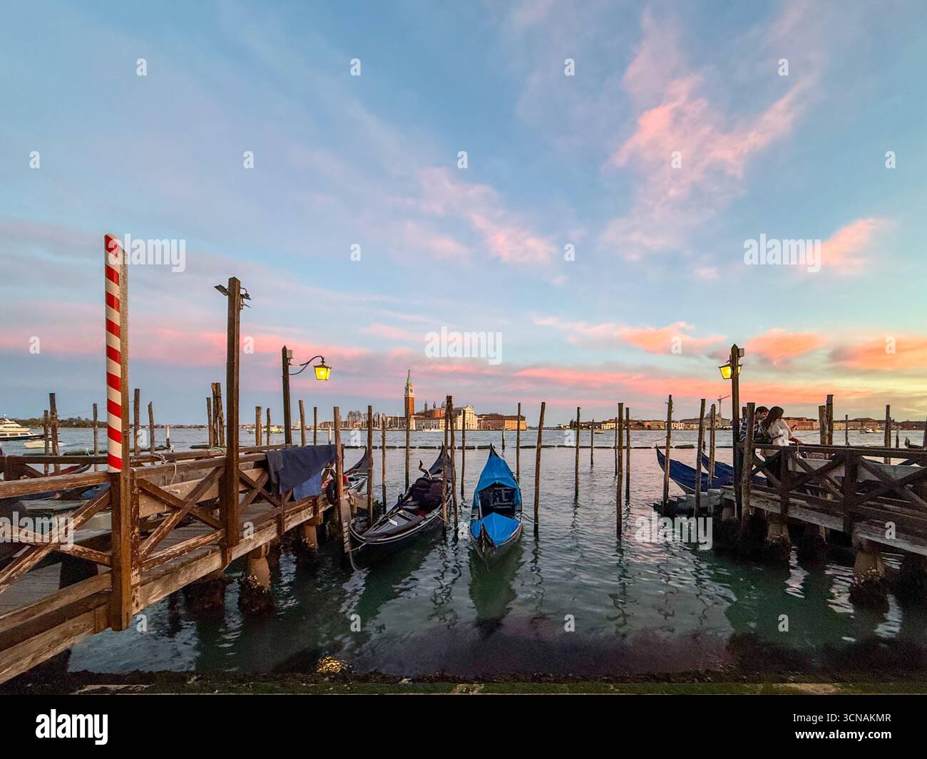 Gondolas moored at Riva degli Schiavoni waterfront, with the Islands of San Giorgio Maggiore and Giudecca in the background at sunset, Venice, Italy - Smartphone Captured Stock Image