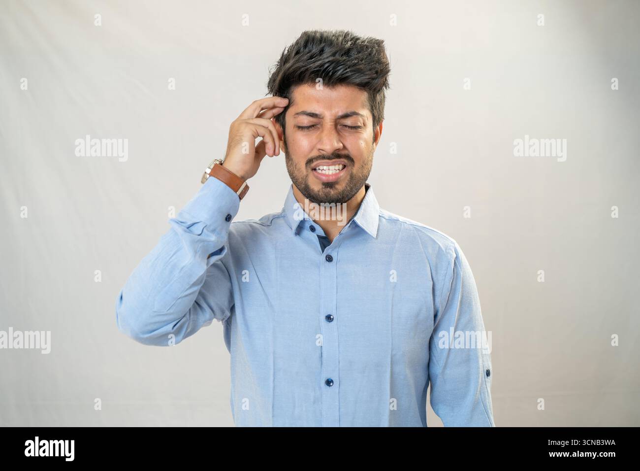 A young man with a serious, thoughtful expression, touching his forehead. Stock Photo