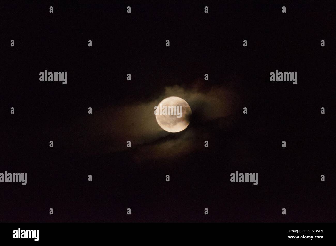 Mesmerising night scene of a Full Moon peeping through thick cloud Stock Photo