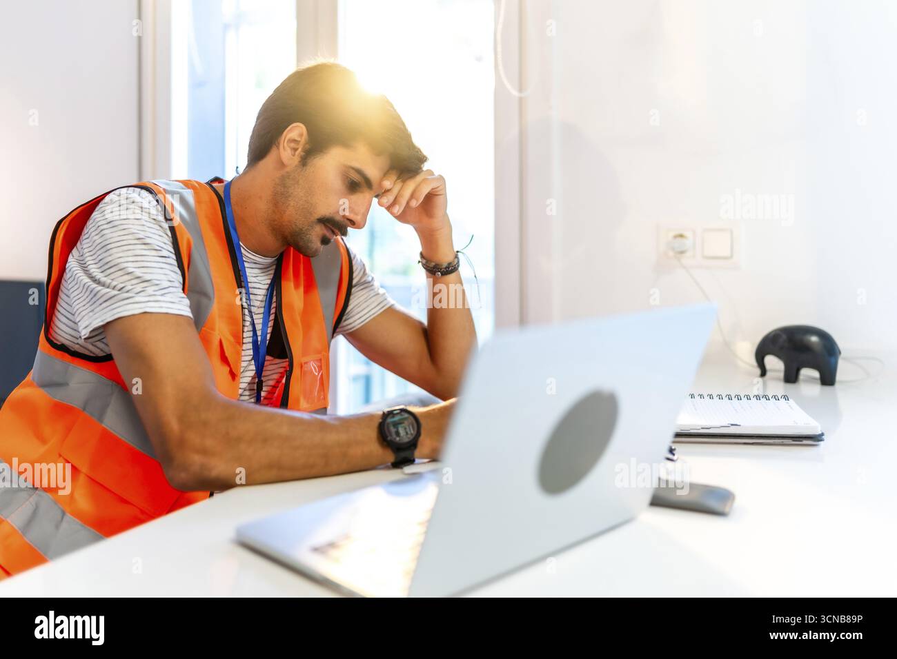 Young construction worker feeling stressed while working remotely from home using laptop, having problems and headache Stock Photo