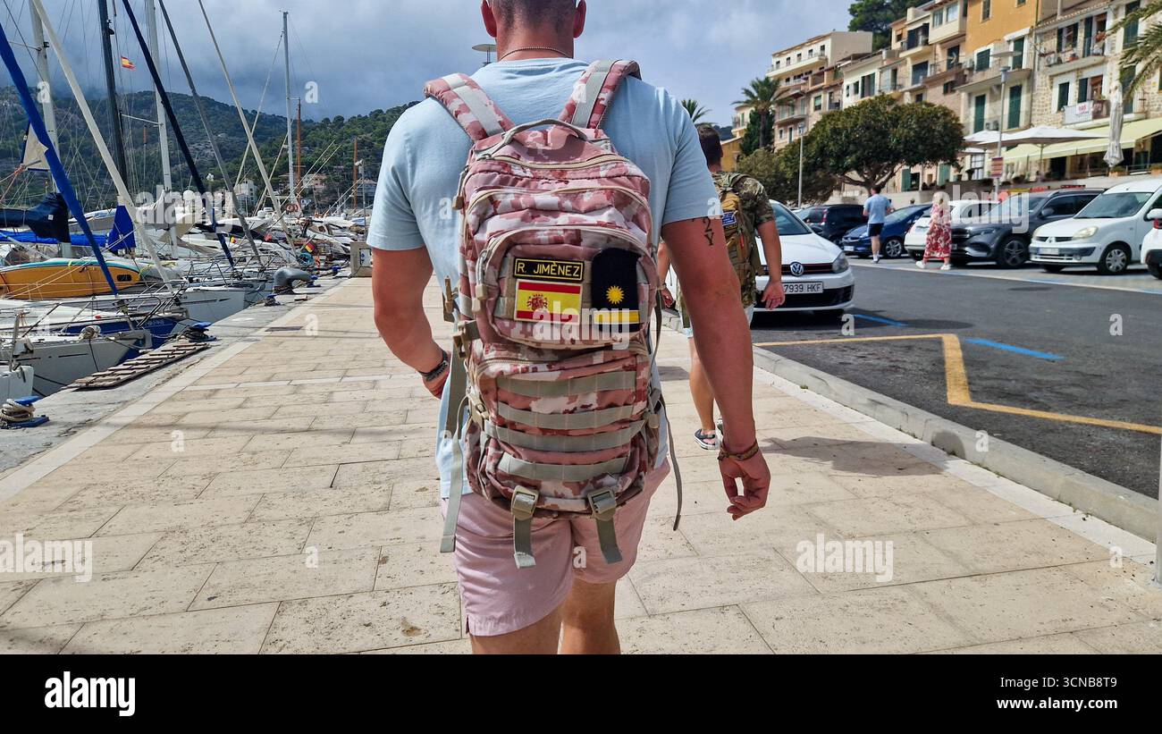 Soller, Spain - September 8 2025: Man walking with camouflage Ejercito de Tierra (Spanish Army) backpack along marina promenade. - Smartphone Captured Stock Image Soller, Spain - September 8 2025: Man walking with camouflage Ejercito de Tierra (Spanish Army) backpack along marina promenade. - Smartphone Captured Stock Image