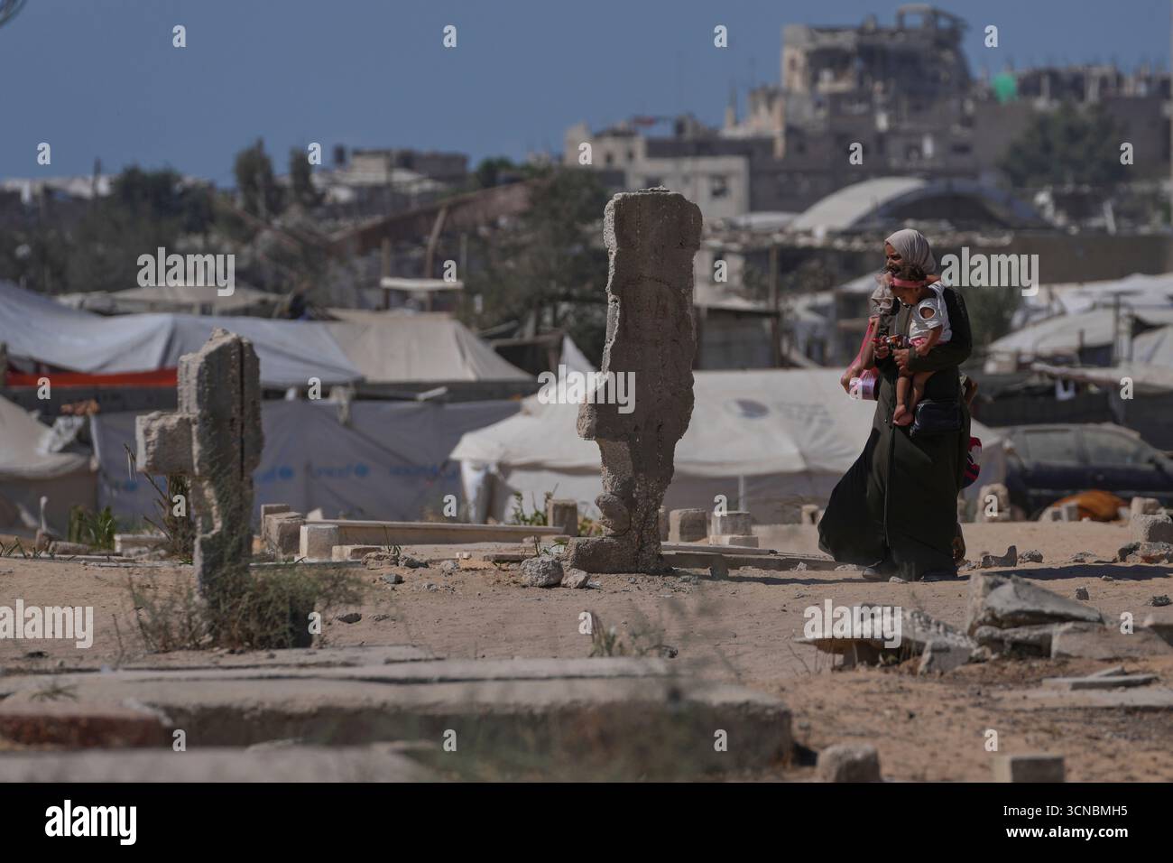 A displaced Palestinian woman carries a child as she walks past ...