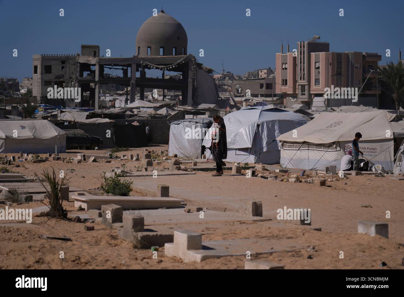 A displaced Palestinian woman carries a child as she walks past ...