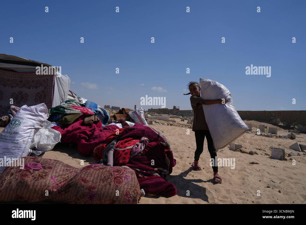 A displaced Palestinian girl carries a bag containing her family's ...