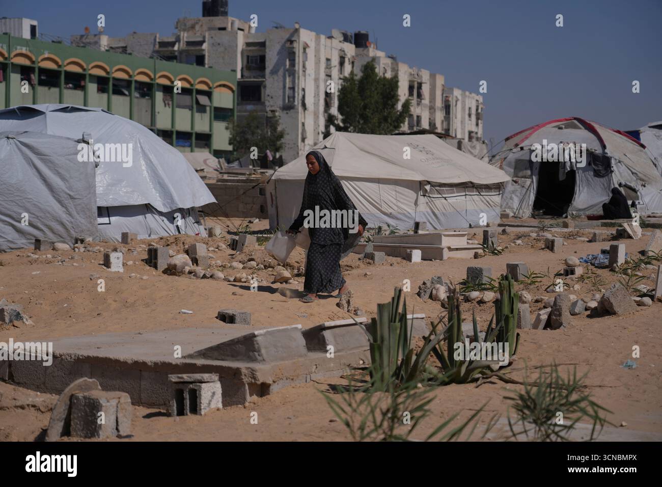 A displaced Palestinian woman walks past makeshift tents set up in a ...
