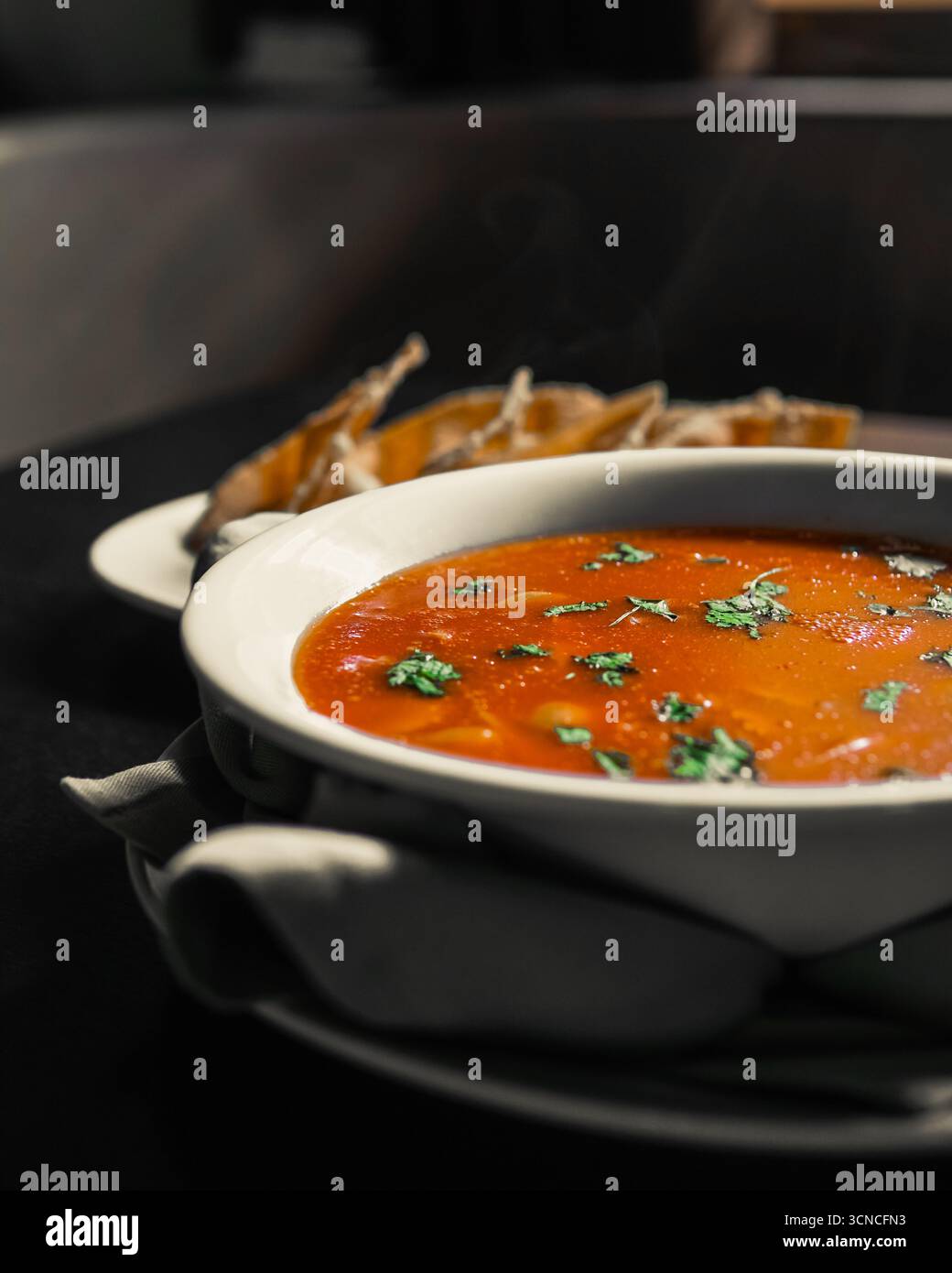 Hot and Flavorful Tomato Soup Garnished with Fresh Herbs, Served with Crispy Bread for a Comforting Meal Stock Photo