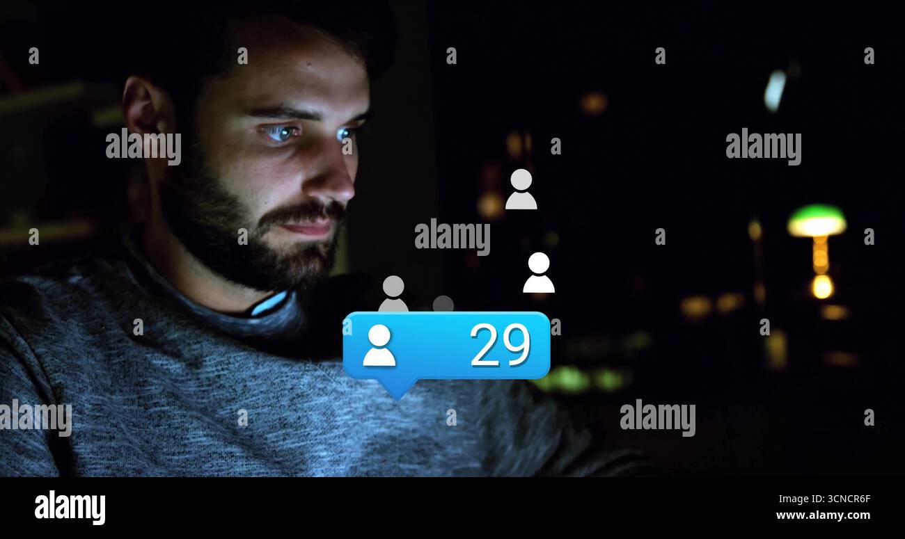 Bearded coder navigating user icons and blue notification bubble on laptop at home at night Stock Photo