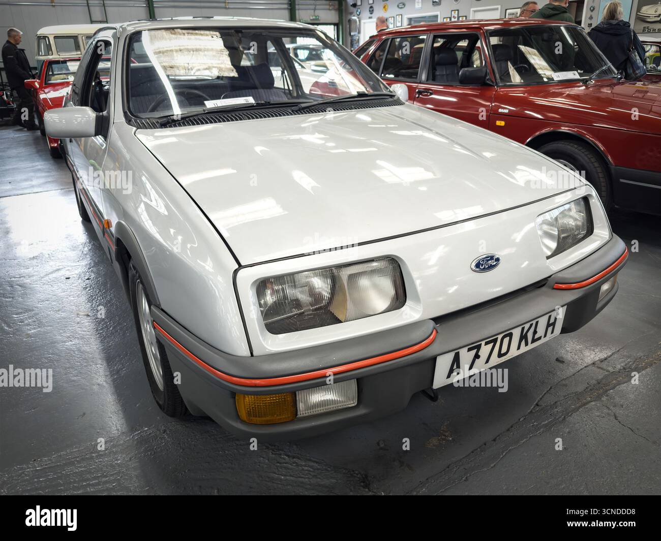 Classic white Ford Sierra XR4 car displayed in a showroom with other vintage vehicles, showcasing its retro design and preserved condition - Smartphone Captured Stock Image