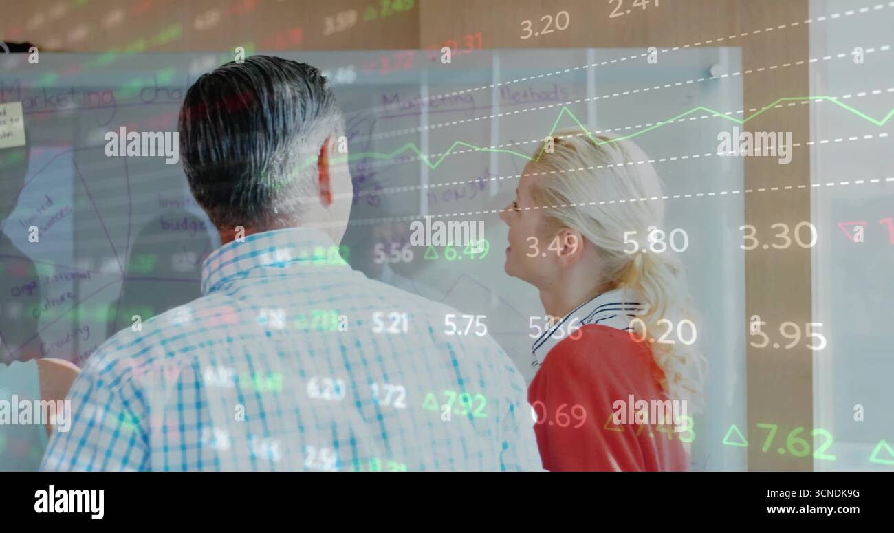 Analyzing coworkers studying data projection on transparent board in office, with sticky notes Stock Photo