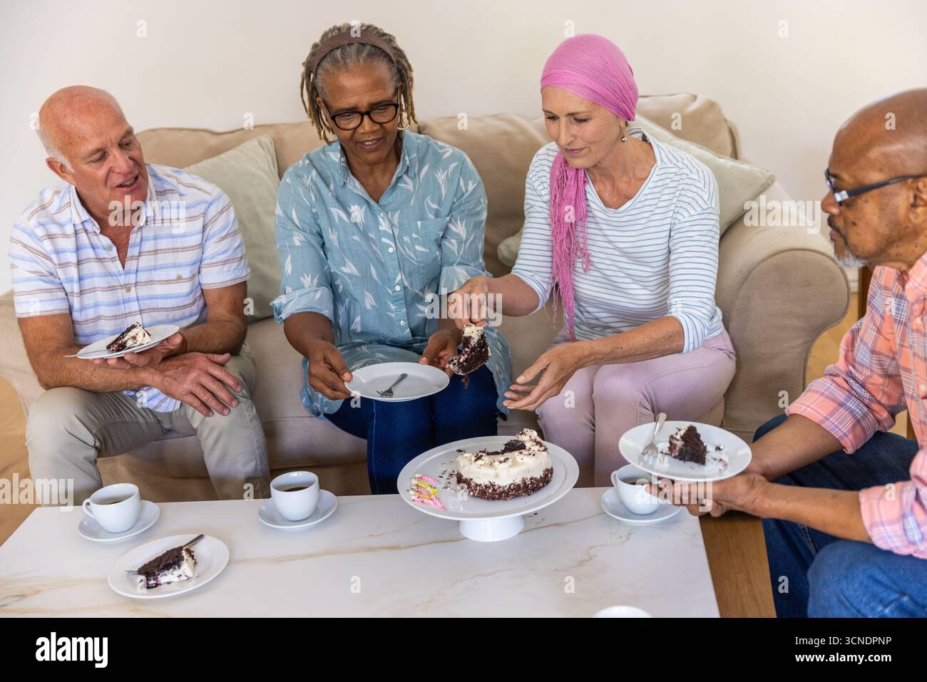 Diverse friends sharing chocolate cake on white coffee table in living room with cups Stock Photo
