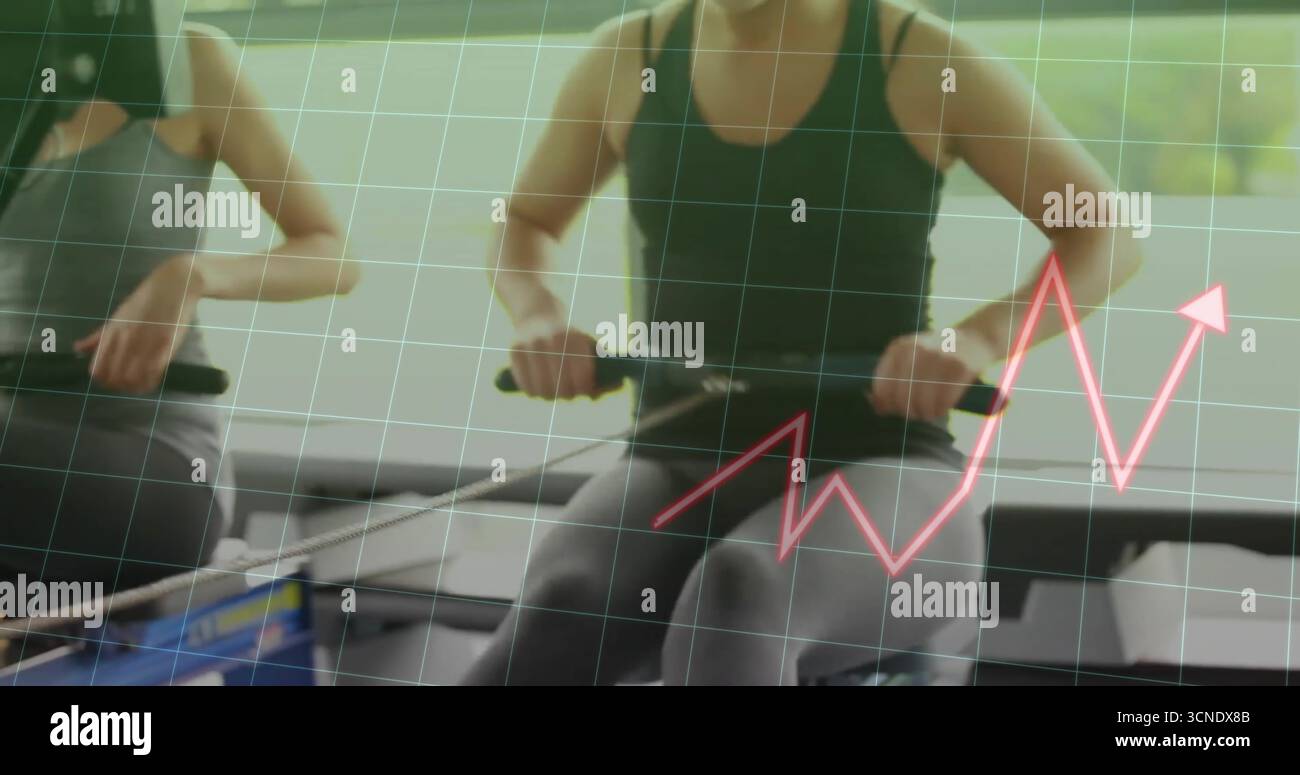 Rowing two athletic women pulling grips and pushing foot straps at gym ...