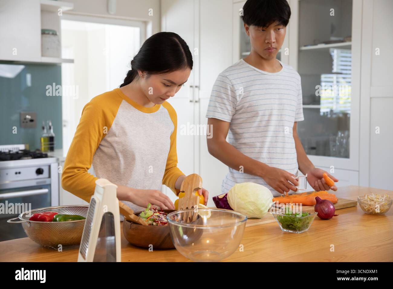 Asian couple mixing salad ingredients in bowl and slicing carrots on home kitchen island Stock Photo