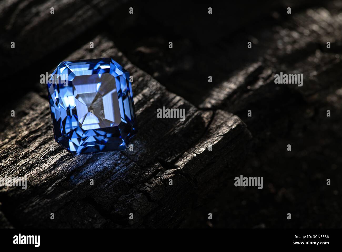 A blue gemstone sits on a rock. The stone is shiny and has a blue hue. The rock is dark and rough, giving the stone a sense of weight and solidity. Th Stock Photo
