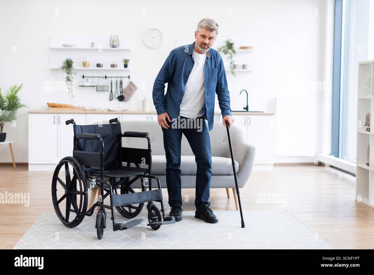 Disabled man practicing walking in modern home using cane for mobility Stock Photo