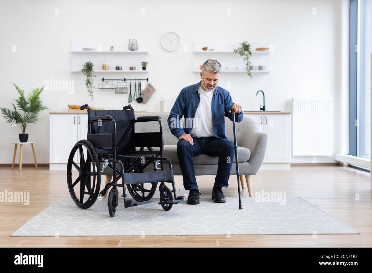 Disabled man practicing walking with a cane in a modern apartment setting Stock Photo
