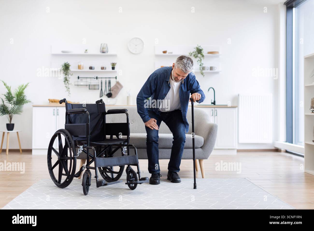 Disabled man practicing walking with cane assistance in home interior setting Stock Photo