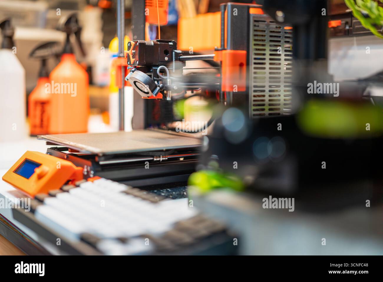 3D printer workspace orange components technology setup with visible extruder, control panel and heated bed in modern fabrication environment Stock Photo
