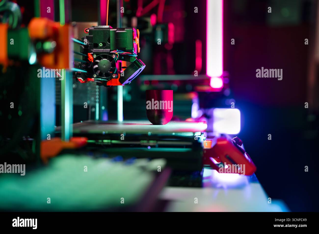 3D printing process neon light modern fabrication showing active 3D printer creating object under colorful studio lighting in high-tech workspace Stock Photo