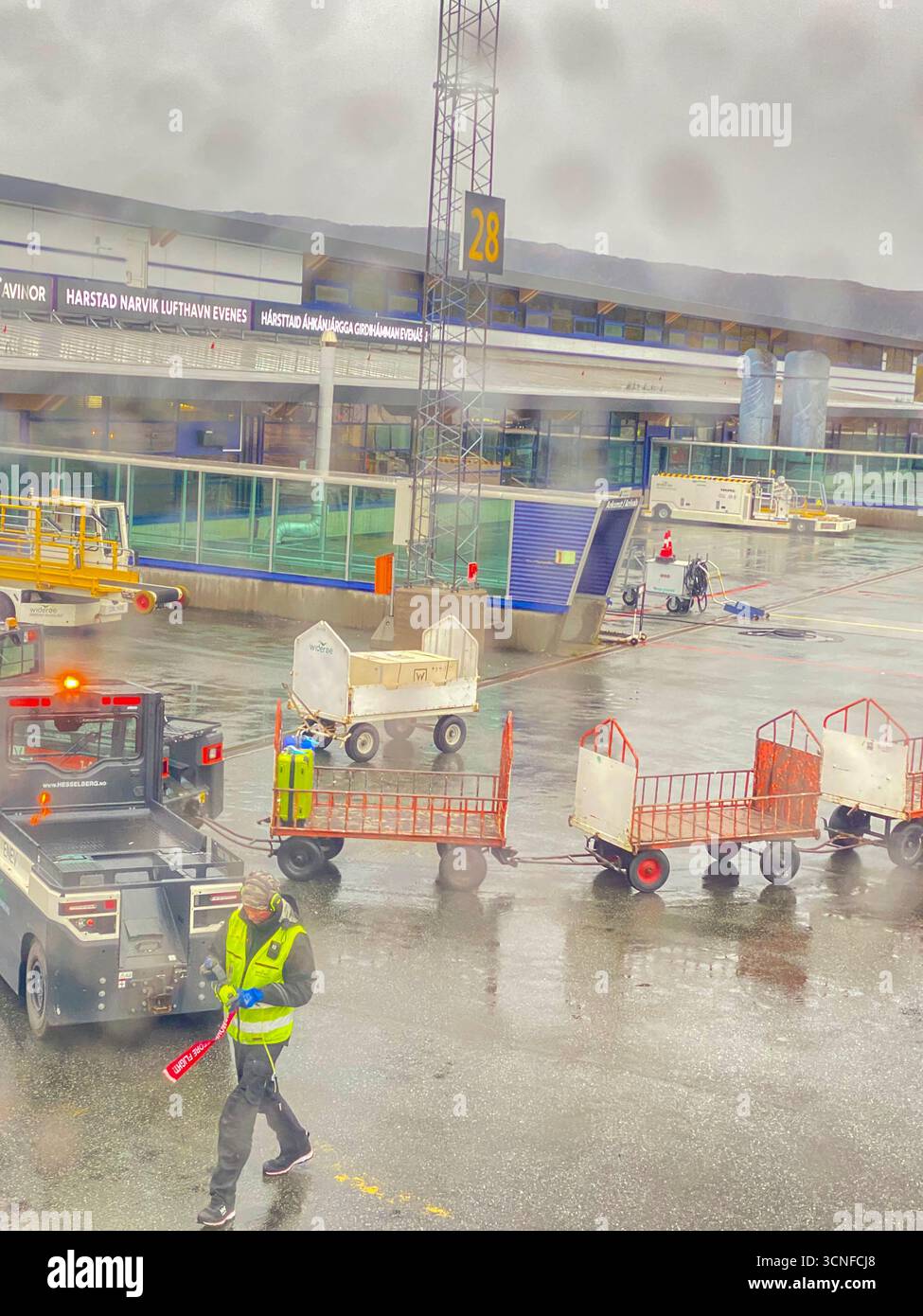 Through the aircraft passenger window of airport ground staff working in the pouring rain at Harstad-Narvik Airport is an international airport locate - Smartphone Captured Stock Image