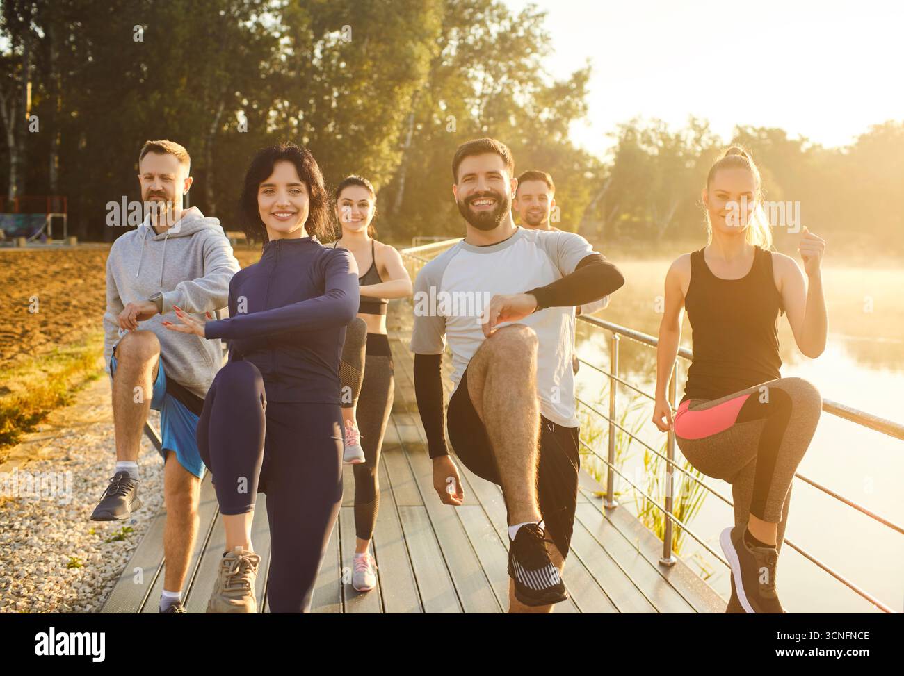 Team of athlets doing exercises outdoors, raising legs, demonstrating strething abilities Stock Photo