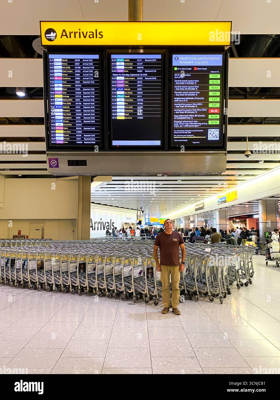 A man reads a large, overhead arrivals board at London Heathrow Airport Terminal 4 - Smartphone Captured Stock Image