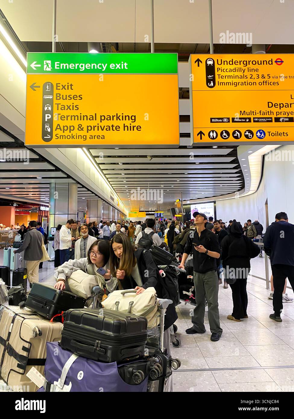 Large, yellow information signs give people directions in arrivals at London Heathrow Airport Terminal 4 in England, UK - Smartphone Captured Stock Image