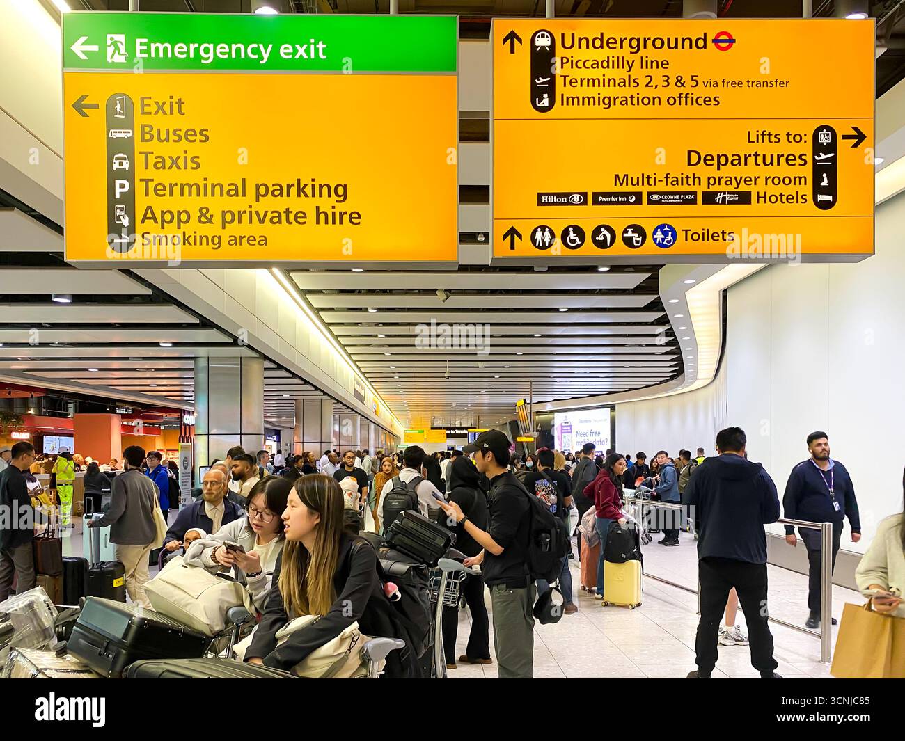 Large, yellow information signs give people directions in arrivals at London Heathrow Airport Terminal 4 in England, UK - Smartphone Captured Stock Image