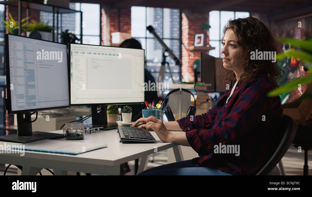 Smiling woman using programming languages on PC in IT startup office to build applications. Upbeat programmer using computer in software development agency to code, camera A Stock Photo