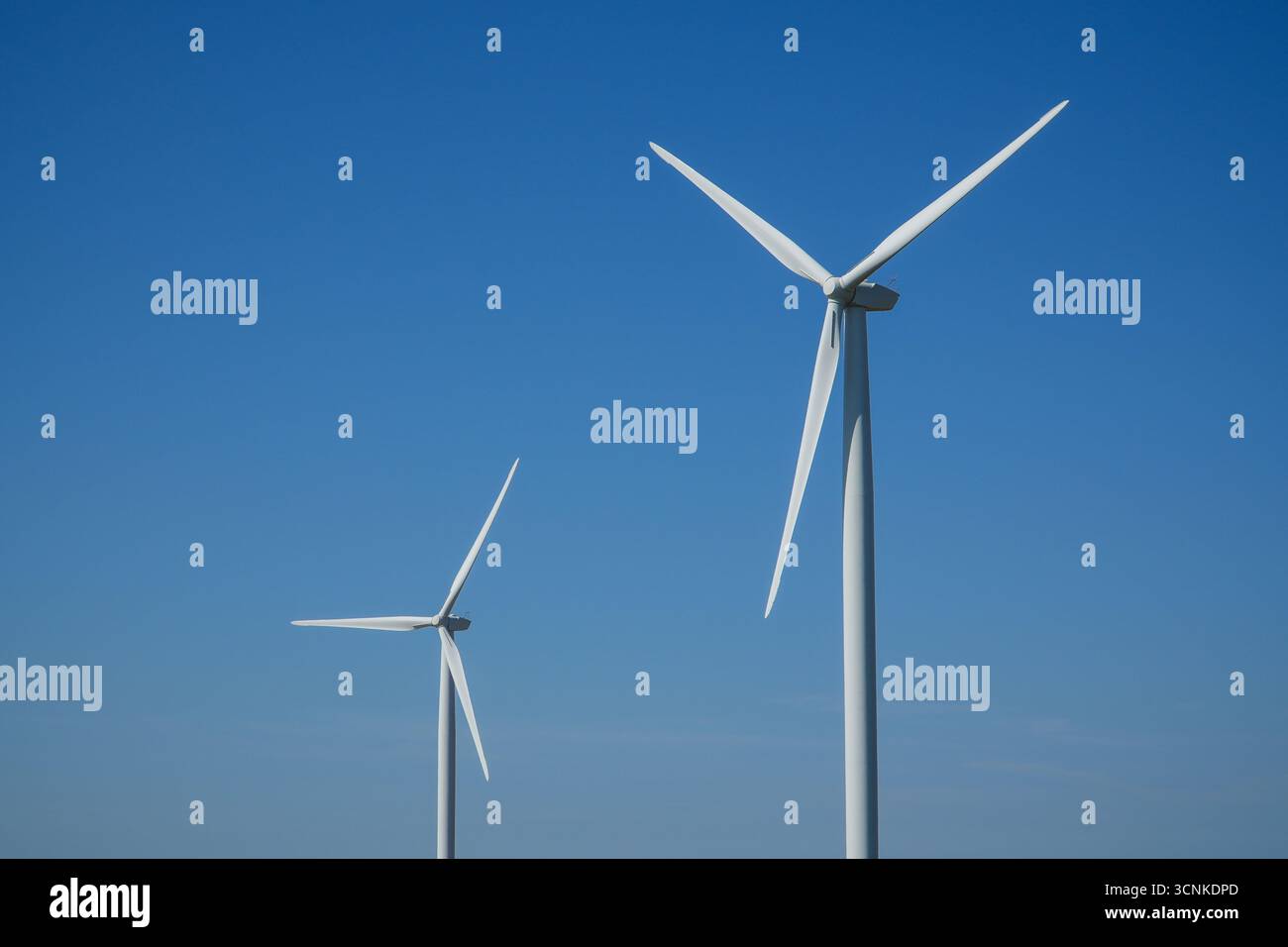 Two wind turbines stand against a clear blue sky, symbolizing ...