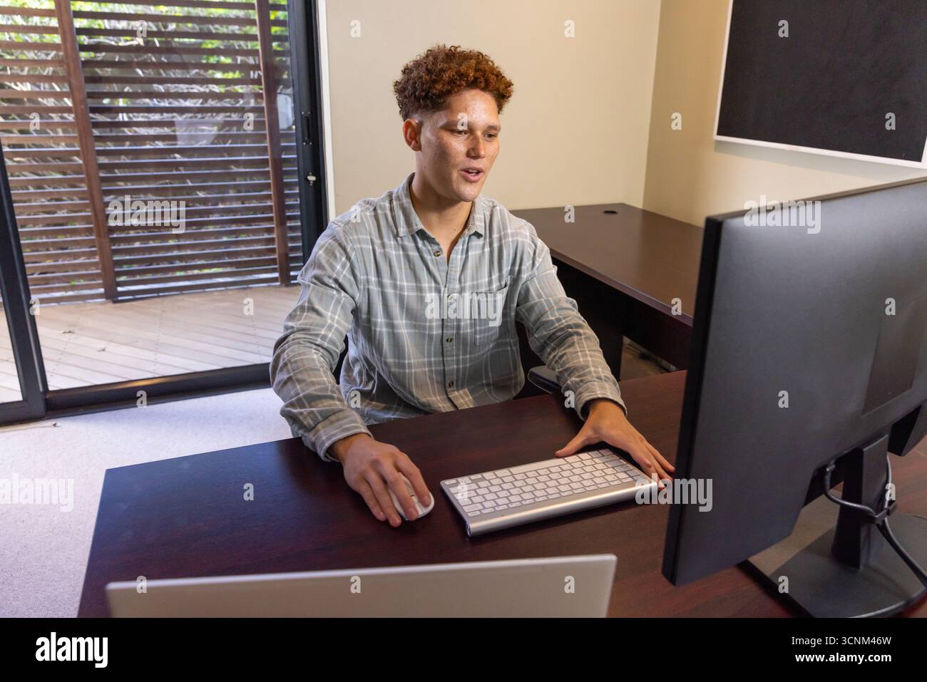 Man working at desk on computer while typing on keyboard, using mouse in home office Stock Photo