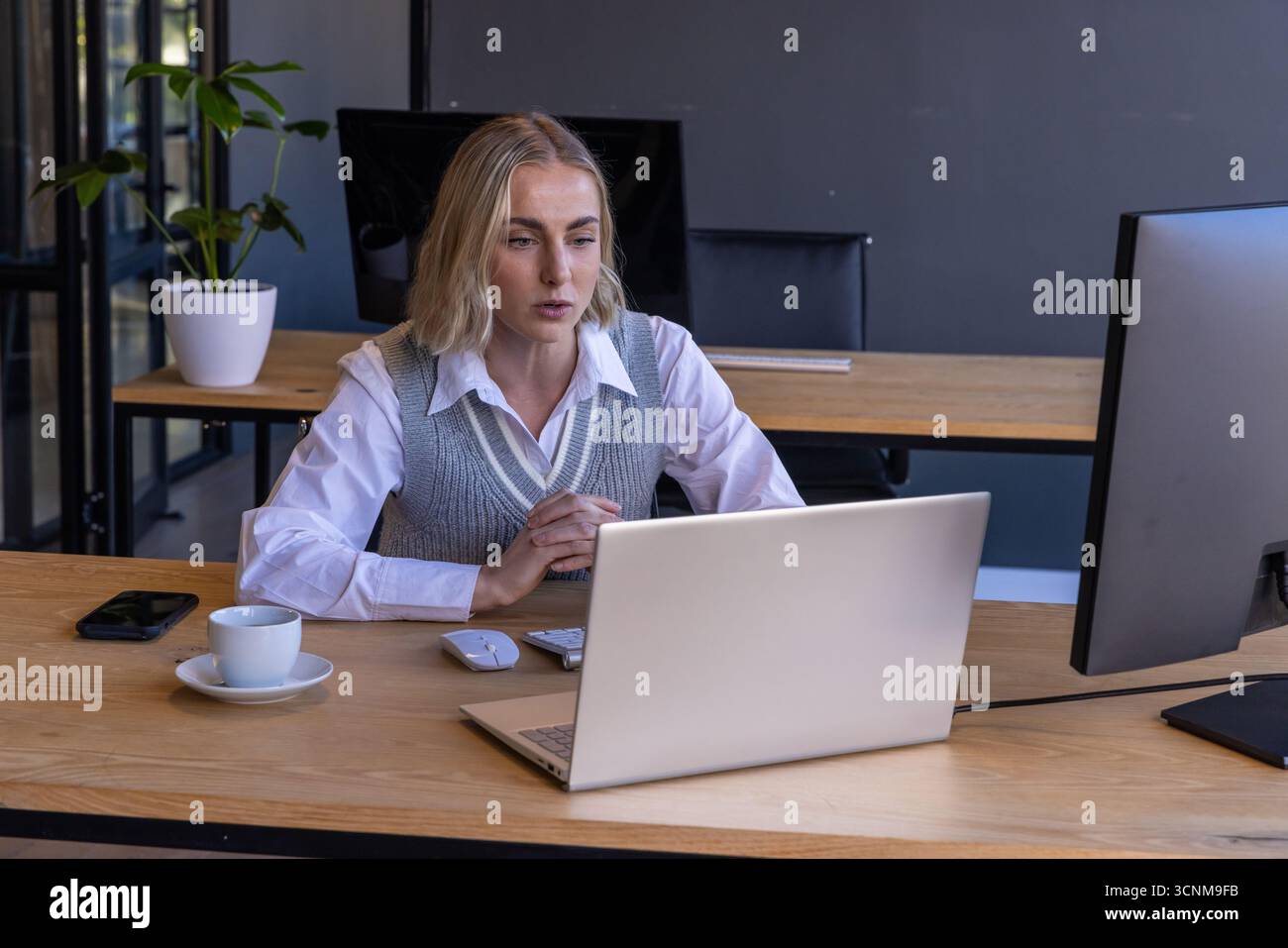 Woman in business attire working on laptop at office desk with coffee ...