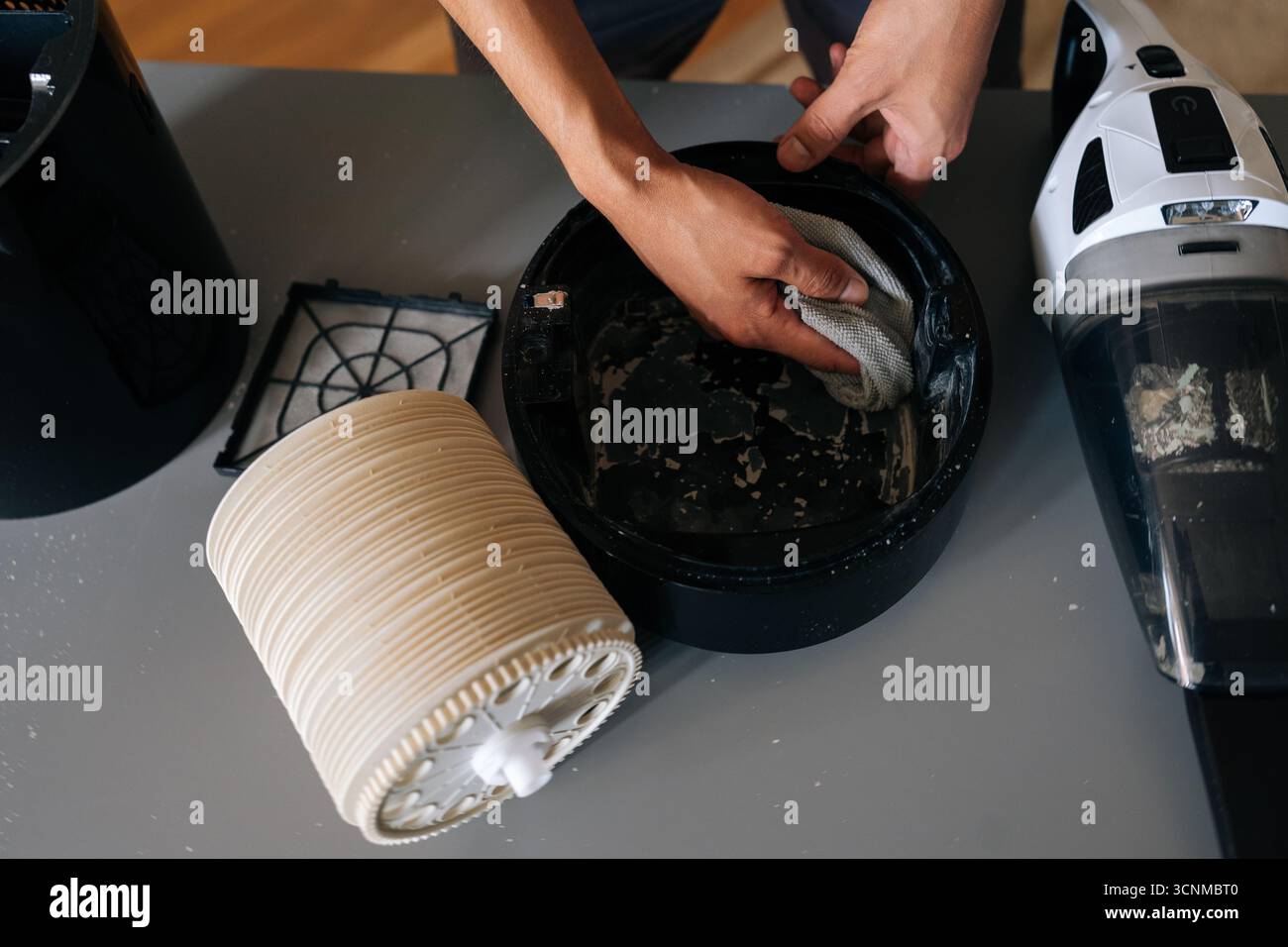 Close-up top view of technician carefully cleaning inside of air humidifier using cloth, with vacuum cleaner nearby to remove dust and debris. Stock Photo