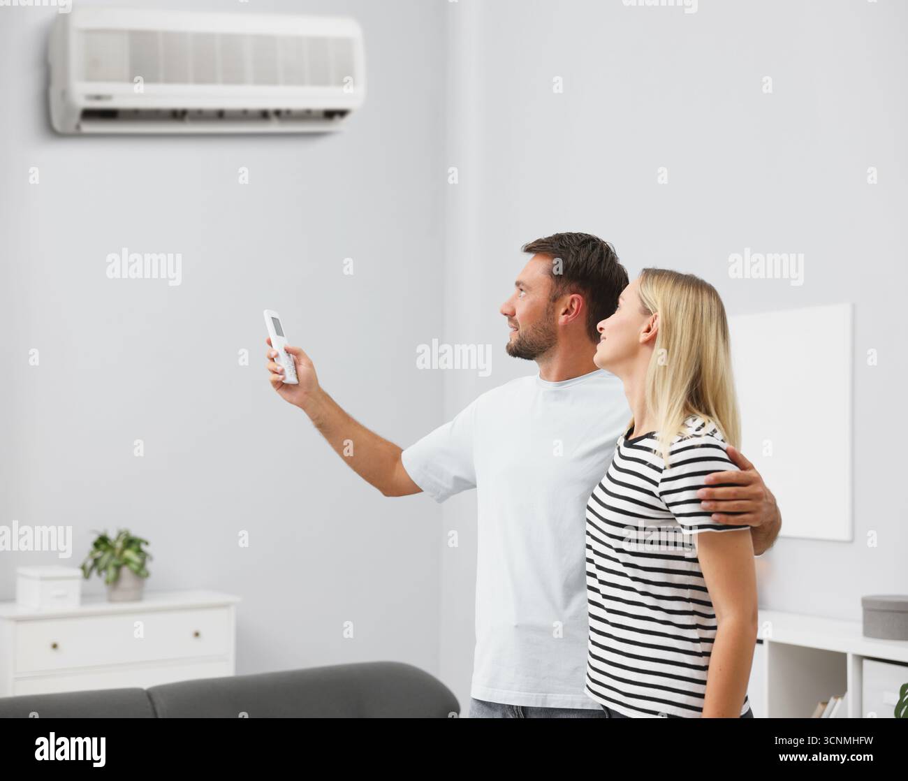 Couple using remote to control air conditioner at home Stock Photo