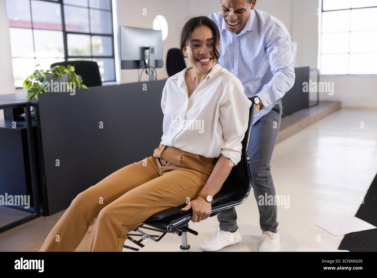 Diverse coworkers in office pushing rolling chair near monitors, desk ...