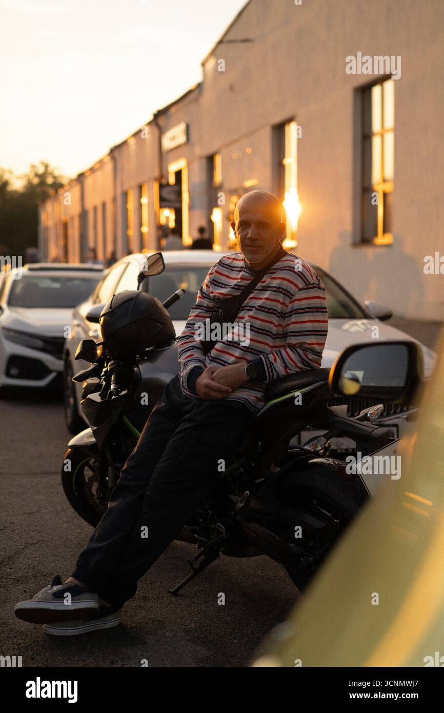 Man on a motorcycle with a sunset background, wearing a striped shirt Stock Photo