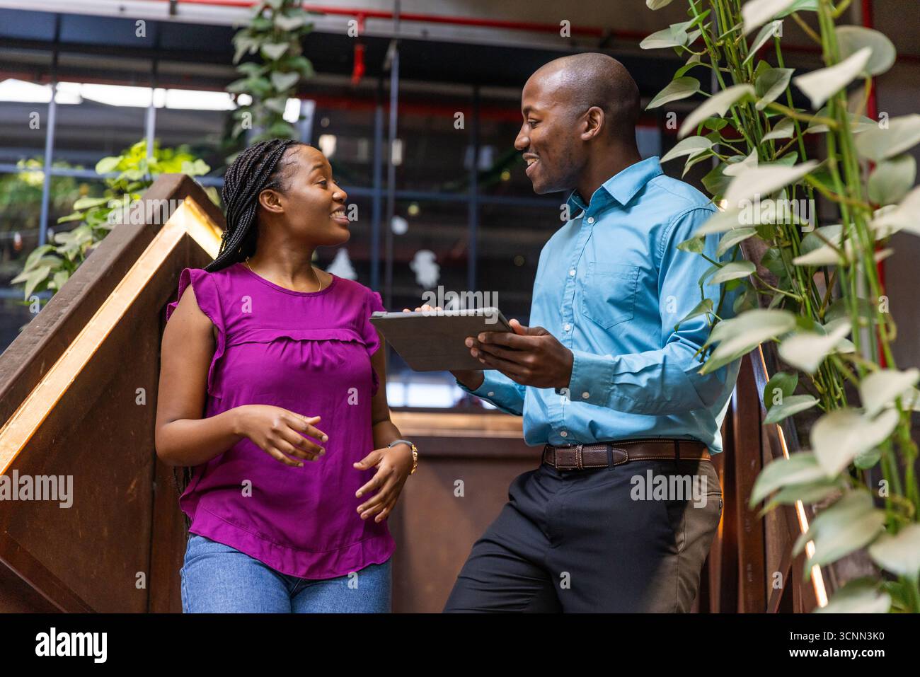 African american colleagues standing on stair with plants discussing data on tablet Stock Photo