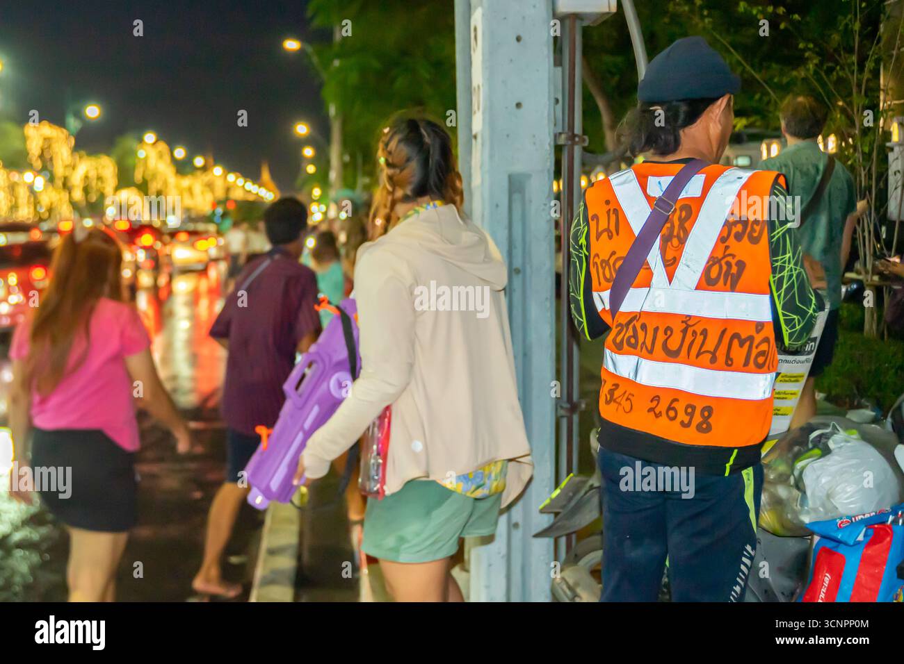Person wearing a high-visibility vest with Thai text, traffic volunteer, on a busy street at night in Bangkok, Thailand. Stock Photo