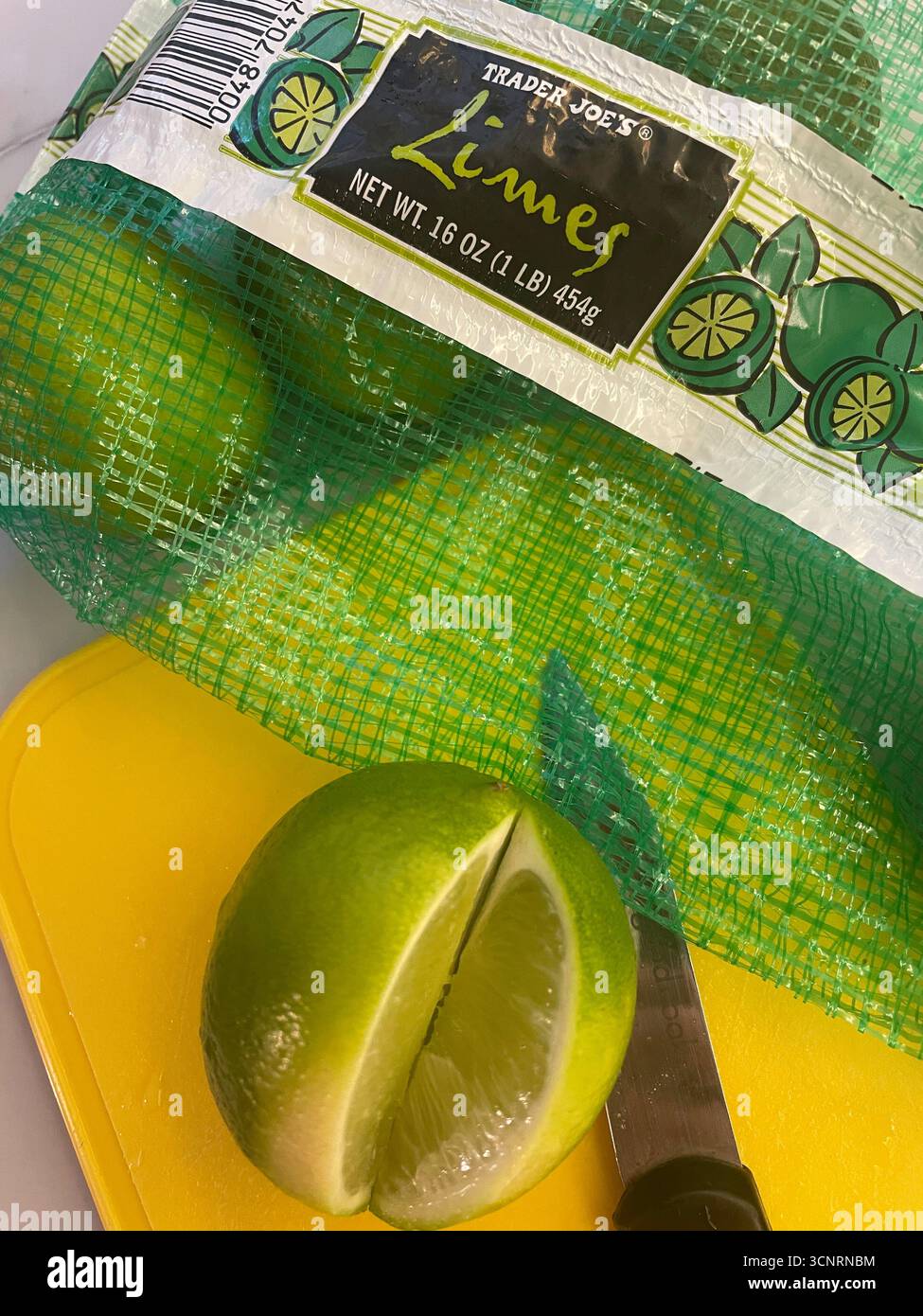 Still life of a bag of Trader Joe's limes on a yellow cutting board and a sliced lime, 2025, United States Stock Photo