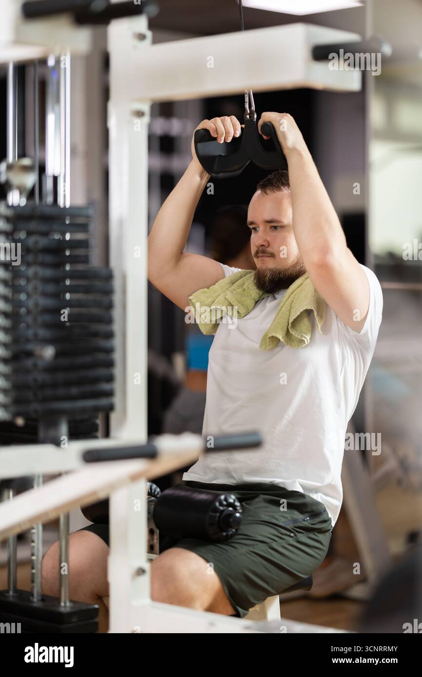 Man in gym performs exercises for arm muscles using cable crossover ...