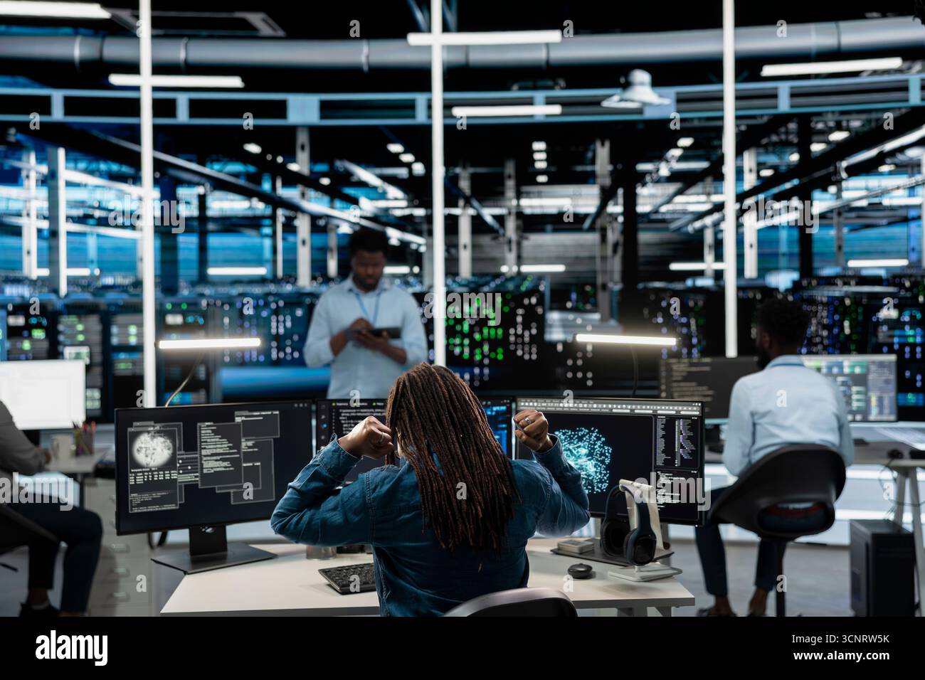 Fatigued data center worker stretching at desk, using machine learning algorithms to analyze datasets. Tired server farm engineer relaxing muscles, using AI to recognize data patterns Stock Photo