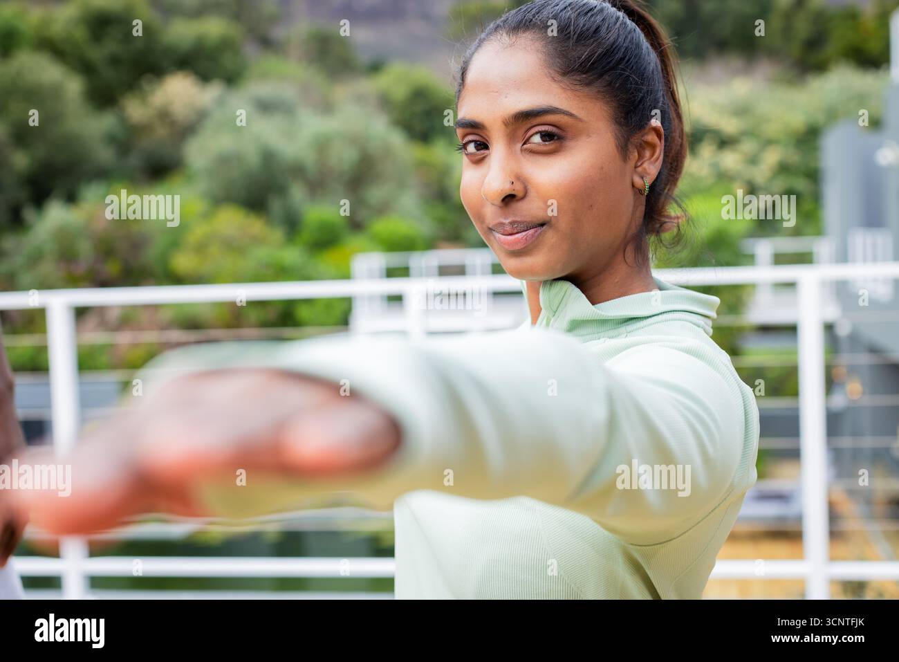 Indian woman stretching arm wearing green athletic top on balcony with ...