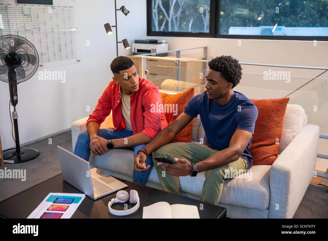 Diverse male colleagues discussing design concepts over laptop and phone mockups in office lounge Stock Photo
