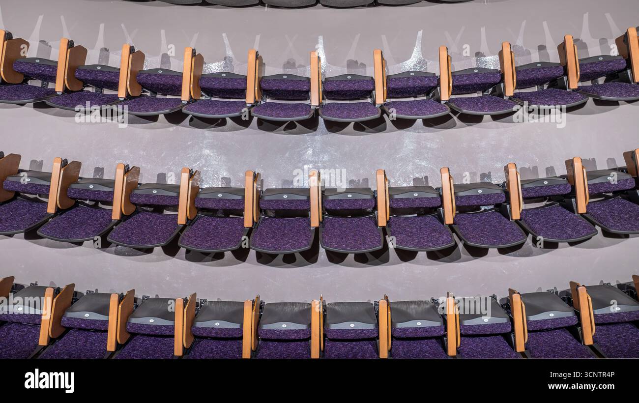 Purple padded auditorium seats, chairs with gray concrete floor, in an ...
