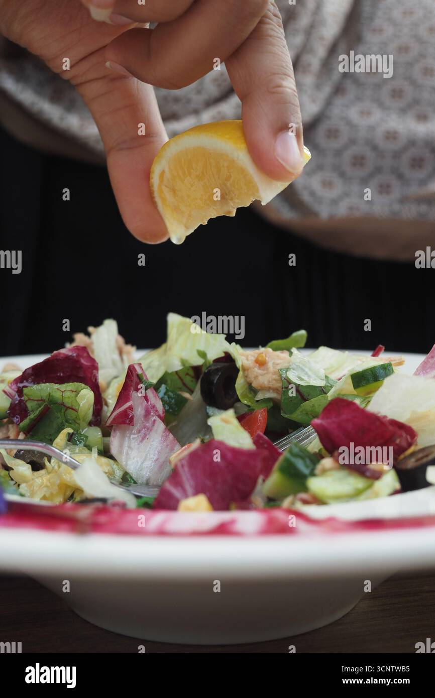 Squeezing lemon over fresh salad in outdoor setting Stock Photo