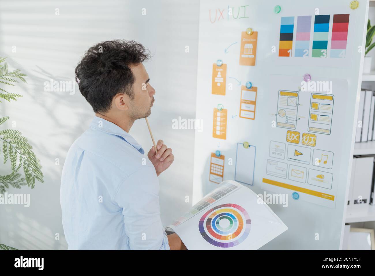 A creative designer is working on UX UI planning, reviewing wireframes, and adjusting color schemes for a mobile application project, showing focus an Stock Photo