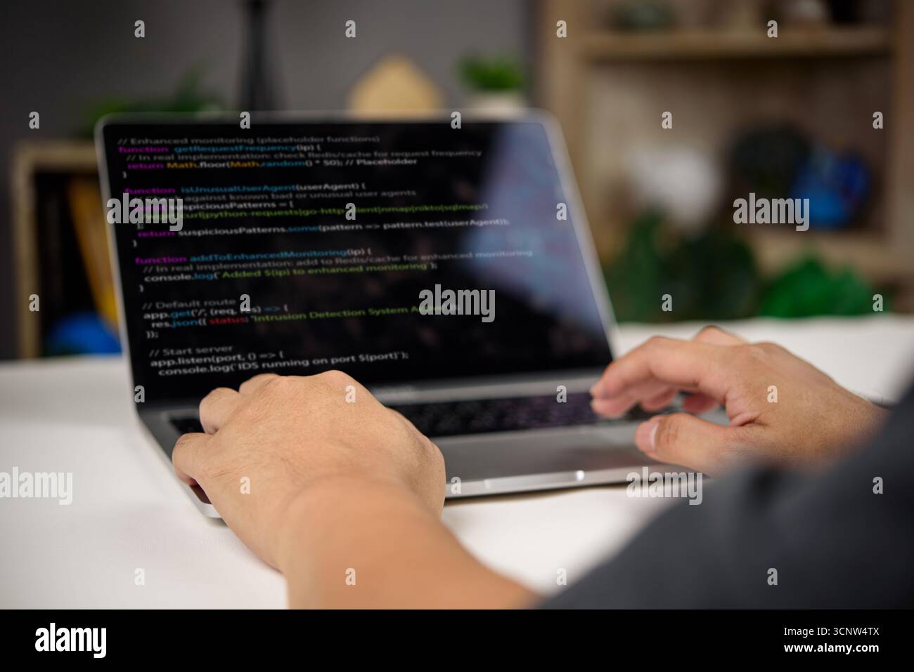 Developer working on intrusion detection system code in JavaScript with real-time monitoring and enhanced security features on laptop. Stock Photo